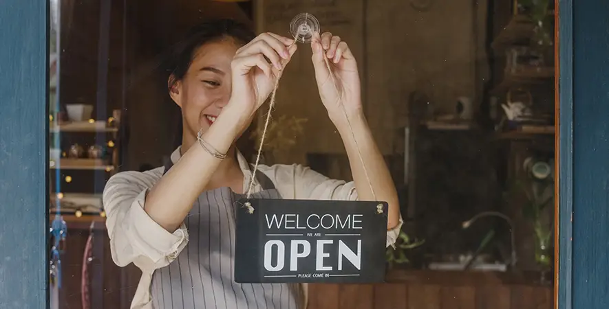Merchant hangs a "Welcome, Open" sign in a coffee shop window.