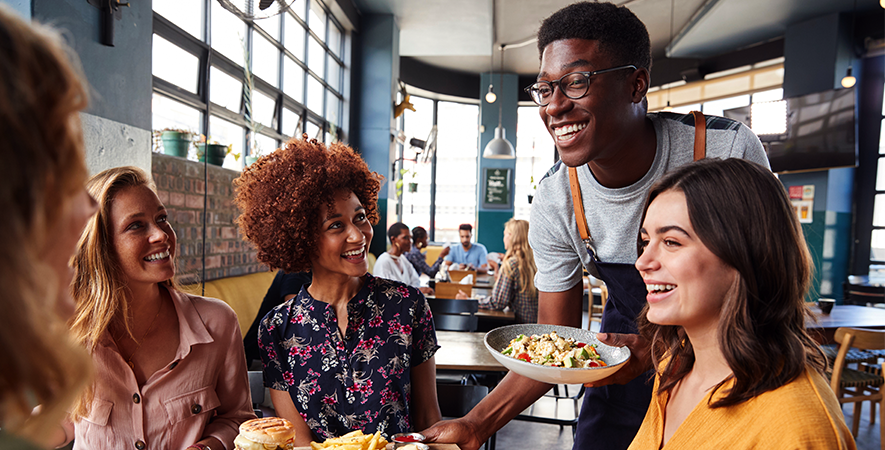 Restaurant staff brings meals to a table of customers.