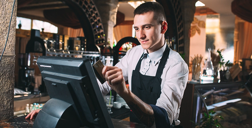 Waiter at a counter POS system swiping a credit card.