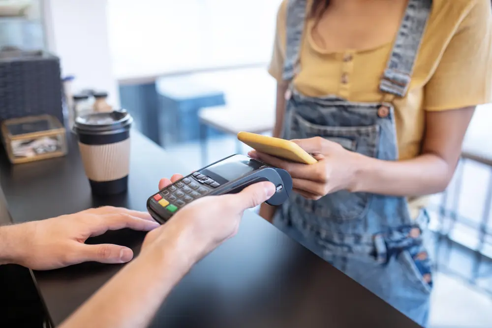 A merchant holds a POS machine for a customer to complete a smartphone transaction.