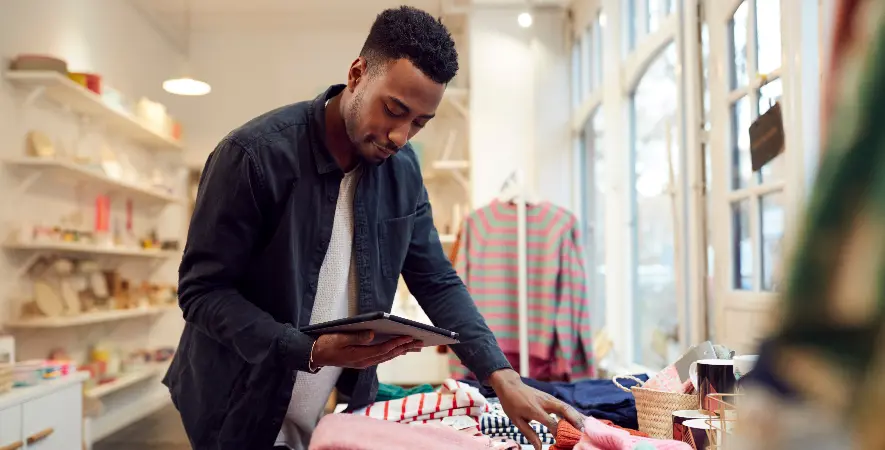 The clothing store owner checks inventory with his payment processing system, confident in his decision between Worldpay vs Sekure.