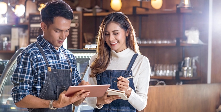 Restaurant owners review their payment processing fees and savings on a tablet with a notepad.