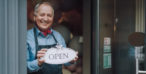 Cheerful gentleman standing in the doorway of cafe and holding open sign