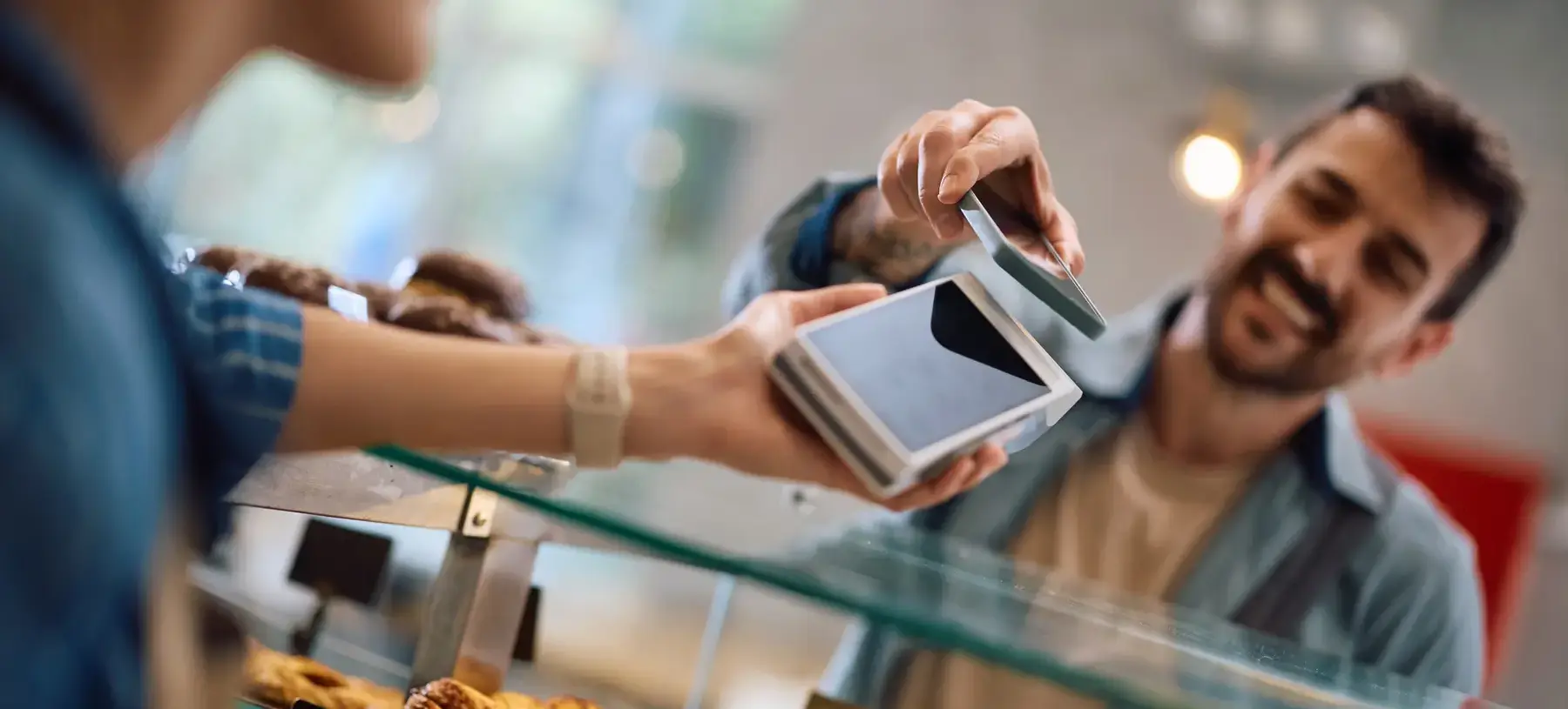 customer in a bakery paying at the counter by tapping their phone to the payment terminal being held by the employee