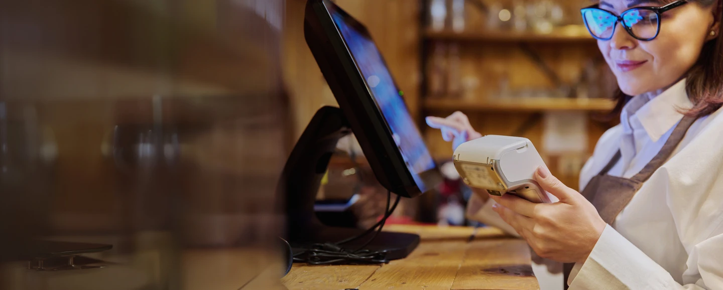 retail store employee holding a handheld payment terminal and punching in informaiton on a touch screen POS