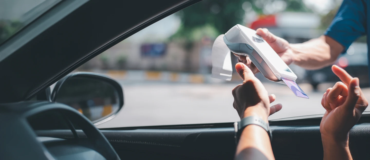 person sitting in their car while an attendant holds a payment terminal for them to pay with their credit card