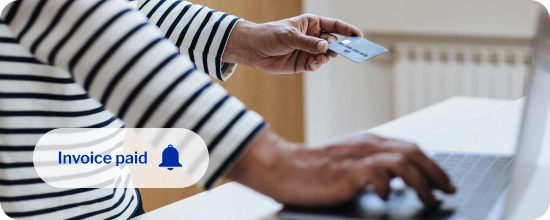 person holding their credit card in their left hand while typing the information into their laptop with their right hand to complete and online sale