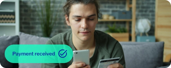 person sitting on a couch in their living room holding their credit card in their left hand and entering the information into their mobile phone in their right hand
