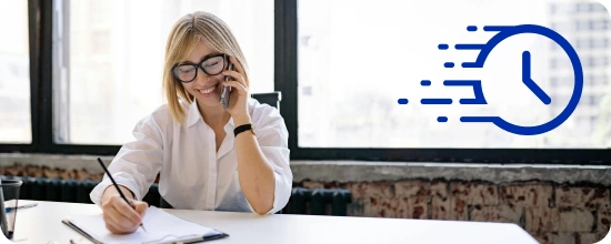 person-in-a-professional office sitting at a desk writing notes in a notepad while talking on the phone and smiling