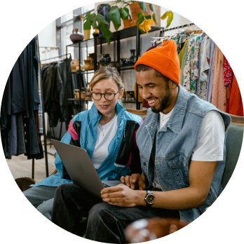clothing store business partners sitting together on a couch looking at a laptop and discussing the information