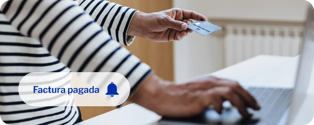 Persona sostiene una tarjeta de crédito con la mano izquierda mientras ingresa los números para completar un pago en línea
