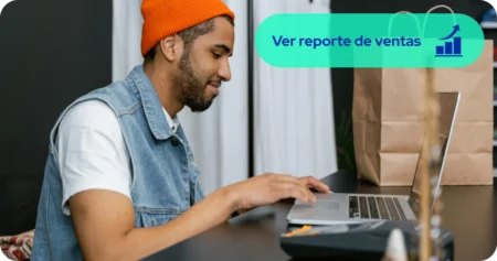 Empleado de boutique revisando inventario y reporte de ventas en computador portátil sobre el mostrador