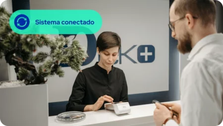 Paciente listo para pagar con su teléfono mientras recepcionista ingresa valor en terminal de pago